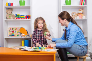 Pediatric therapist guiding a young child through activities to help them play, learn, and do daily tasks independently in a calm therapy room