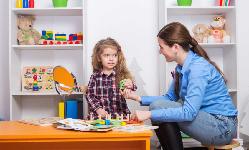 Pediatric therapist guiding a young child through activities to help them play, learn, and do daily tasks independently in a calm therapy room
